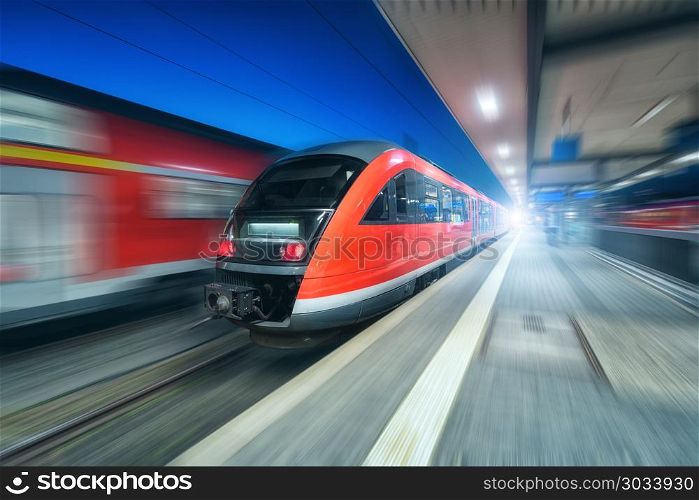 High speed train in motion on the railway station at night. Modern intercity train on the railway platform. Industrial. Passenger commuter red train with motion blur effect. Railroad. Railway travel. High speed train in motion on the railway station at night