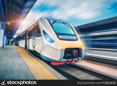 High speed train in motion on the railway station at sunset. Modern intercity passenger train with motion blur effect on the railway platform. Industrial. Railroad in Europe. Commercial transportation. High speed train in motion on the railway station at sunset