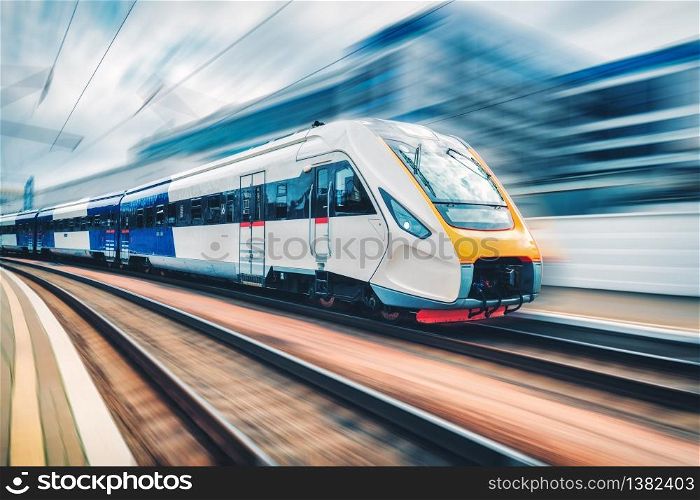 High speed train in motion on the railway station at sunset. Modern intercity passenger train with motion blur effect on the railway platform. Industrial. Railroad in Europe. Commercial transportation. High speed train in motion on the railway station at sunset