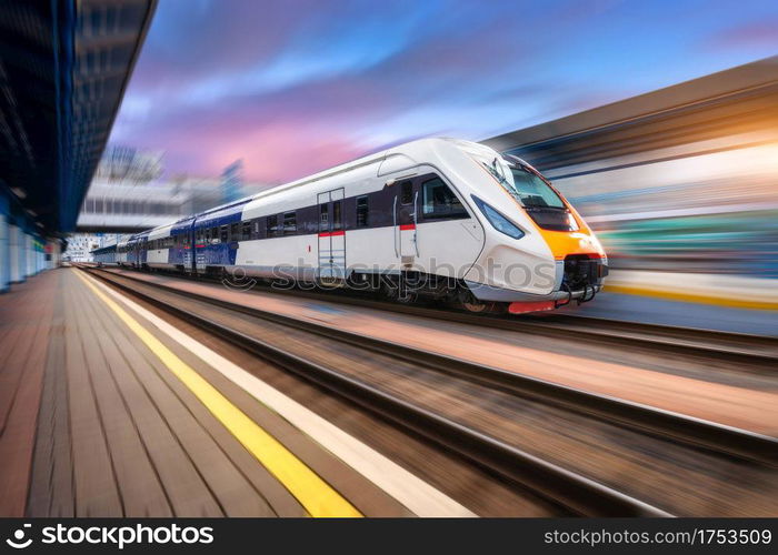 High speed train in motion on the railway station at sunset. Fast moving modern passenger train on railway platform. Railroad with motion blur effect. Commercial transportation. Front view. Concept