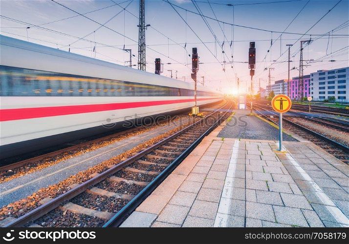 High speed train in motion on the railway station at sunset. Moving blurred modern intercity train on the railway platform in Europe. Passenger railway transportation. Railroad in the evening. Travel