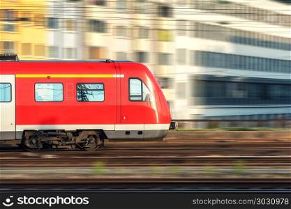 High speed train in motion on the railway station at sunset in Germany. Modern intercity train on the railway platform with motion blur effect. Industrial landscape with passenger train on railroad. High speed red train in motion at sunset