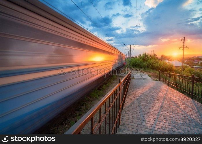 High speed train in motion on the railway station at sunset in summer. Moving modern intercity passenger train, railway platform, green trees and sunlight. Railroad in Urkaine. Railway transportation. High speed train in motion on the railway station at sunset