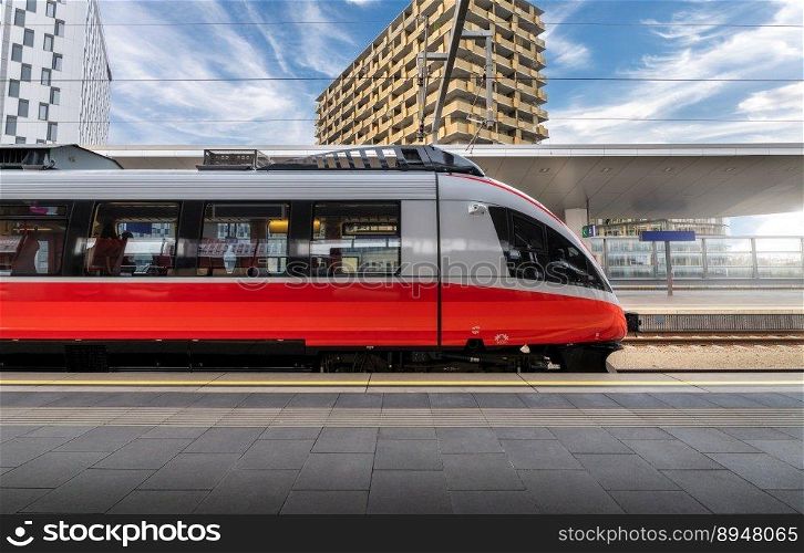 High speed train on the train station at sunset in Vienna, Austria. Beautiful red modern intercity passenger train on the railway platform, buildings. Side view. Railroad. Commercial transportation. High speed train on the train station at sunset in Vienna