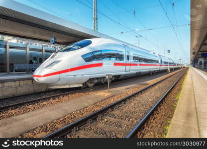 High speed white train on the railway station at sunset. Nuremberg, Germany. Modern intercity train on the railway platform. Industrial. Amazing passenger train on railroad. Transportation. Europe. High speed white train on the railway station