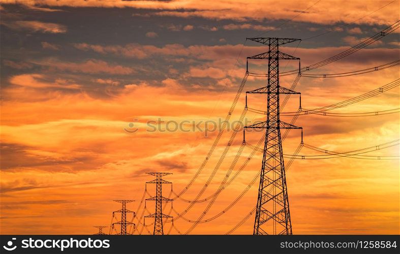 High voltage electric pole and transmission line in the evening. Electricity pylons at sunset. Power and energy. High voltage grid tower with wire cable at distribution station with orange sunset sky.
