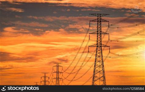 High voltage electric pole and transmission line in the evening. Electricity pylons at sunset. Power and energy. High voltage grid tower with wire cable at distribution station with orange sunset sky.