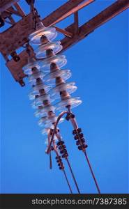 High-voltage electrical insulator made of glass on electric line against the blue sky with copyspace. High-voltage electrical insulator made of glass on electric line against the blue sky