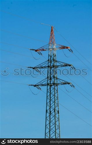 High voltage tower with electricity transmission power lines against blue sky