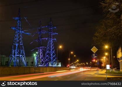 High voltage towers lightened with blue and purple lights in evening with the street lights in foreground, long exposure