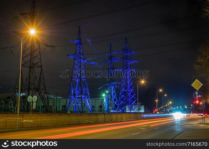 High voltage towers lightened with blue light in evening with the street lights in foreground, long exposure