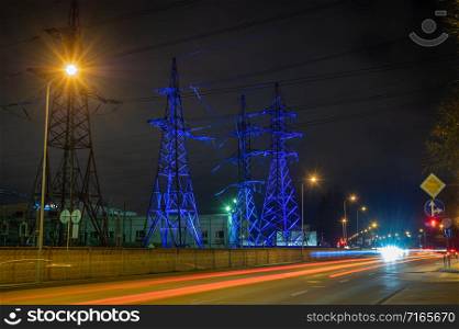 High voltage towers lightened with blue light in evening with the street lights in foreground, long exposure