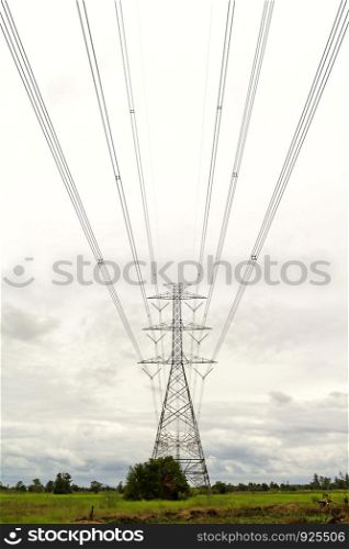 High voltage transmission tower on the ground with gray clouds background.