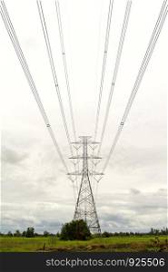High voltage transmission tower on the ground with gray clouds background.