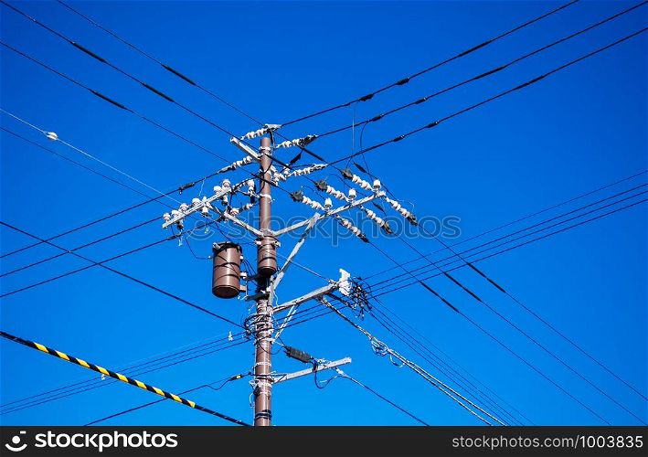 High voltage wires multi direction on electric pole with transformer against bright blue sky