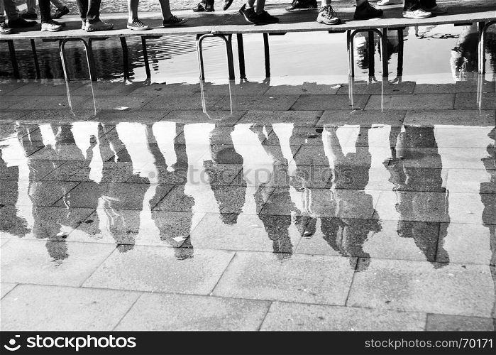High water in Venice - People on foot bridge reflect in a huge puddle on San Marco square in Venice, Italy. Black and white image