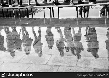 High water in Venice - People on foot bridge reflect in a huge puddle on San Marco square in Venice, Italy. Black and white image