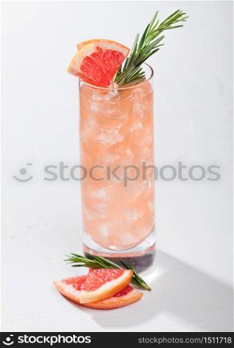 Highball glass of cocktail with red grapefruit and gin with vodka with ice cubes, fruit slice and rosemary on white background.