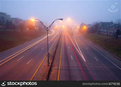 Highway at foggy night with bright trails of light from incoming and outgoing traffic. Transportation, traffic, urbanism and infrastructure concepts.. Highway at foggy night with bright trails of light from incoming and outgoing traffic.