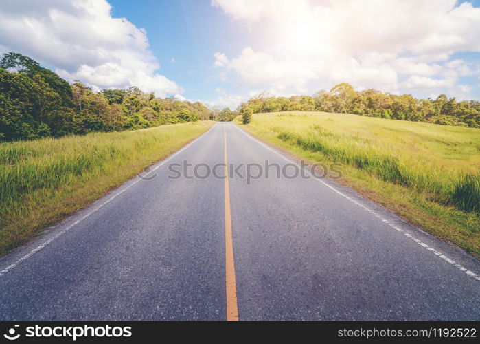 Highway road up hill through green grass field under white clouds on blue sky in summer day. Road trip travel concept.