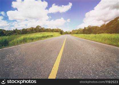Highway road up hill through green grass field under white clouds on blue sky in summer day. Road trip travel concept.