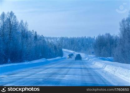Highway through the winter northern forest. Several cars. Traffic on the Forest Winter Road