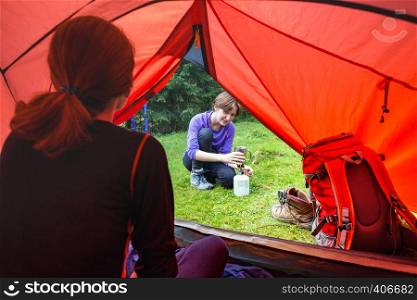 hike and camping life. view from the tent on tourist girl cooks food on a burner