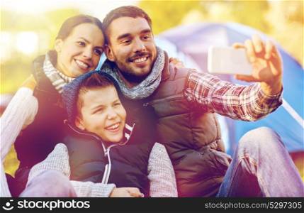 hike, technology and travel concept - happy family with smartphone taking selfie at campsite. family with smartphone taking selfie at campsite