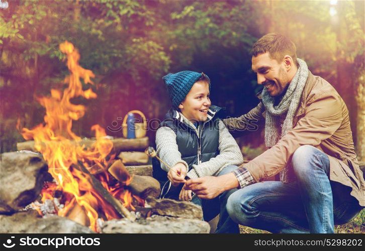 hike, travel and family concept - happy father and son roasting marshmallow over campfire. father and son roasting marshmallow over campfire
