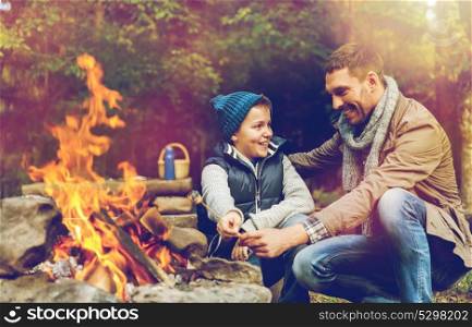 hike, travel and family concept - happy father and son roasting marshmallow over campfire. father and son roasting marshmallow over campfire