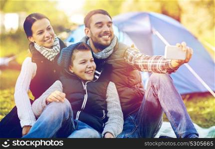 hike, travel and technology concept - happy family with smartphone taking selfie at campsite. family with smartphone taking selfie at campsite