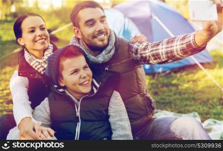hike, travel and technology concept - happy family with smartphone taking selfie at campsite. family with smartphone taking selfie at campsite