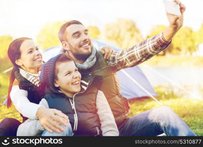 hike, travel and technology people concept - happy family with smartphone taking selfie at campsite. family with smartphone taking selfie at campsite