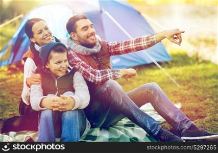 hike, travel, tourism and people concept - happy family over tent at camp site pointing finger to something. happy family with tent at camp site