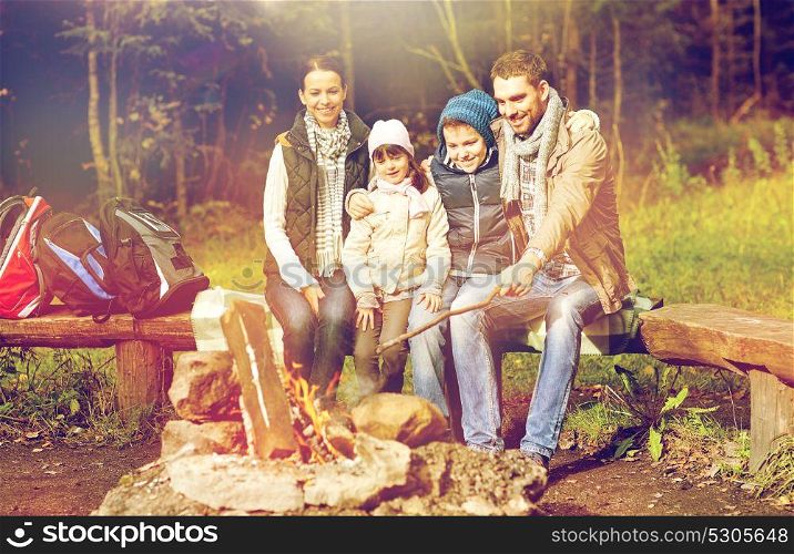 hike, travel, tourism and people concept - happy family sitting on bench at camp fire in woods. happy family sitting on bench at camp fire