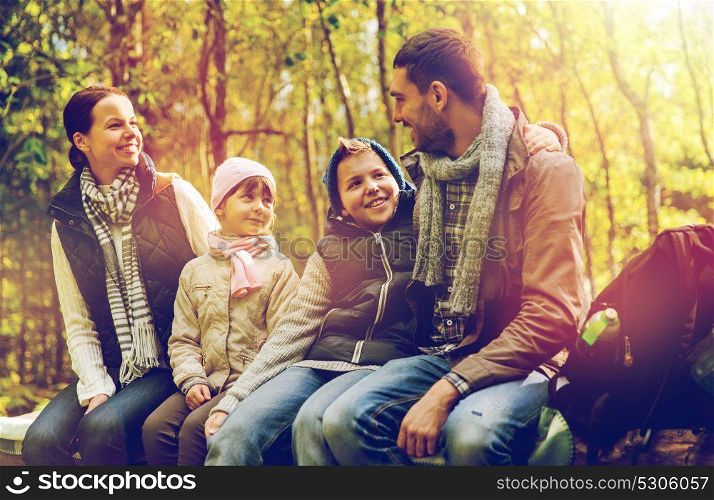 hike, travel, tourism and people concept - happy family sitting on bench and talking at camp in woods. happy family sitting on bench and talking at camp