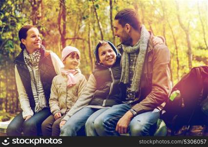 hike, travel, tourism and people concept - happy family sitting on bench and talking at camp in woods. happy family sitting on bench and talking at camp