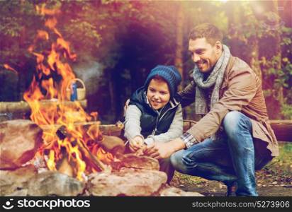 hike, travel, tourism and people concept - happy father and son roasting marshmallow over campfire. father and son roasting marshmallow over campfire