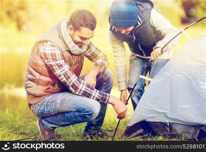 hike, travel, tourism and people concept - happy father and son setting up tent outdoors. happy father and son setting up tent outdoors