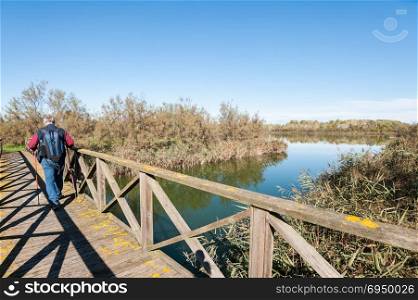 Hiker (60 years old) on a wooden footbridge on the river.
