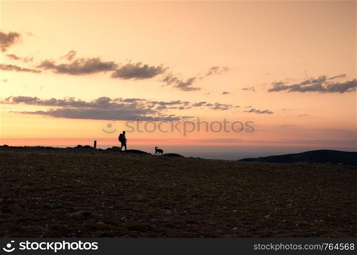 Hiker and his dog walk down the mountain in an amazing sunset. Navacerrada, Spain.