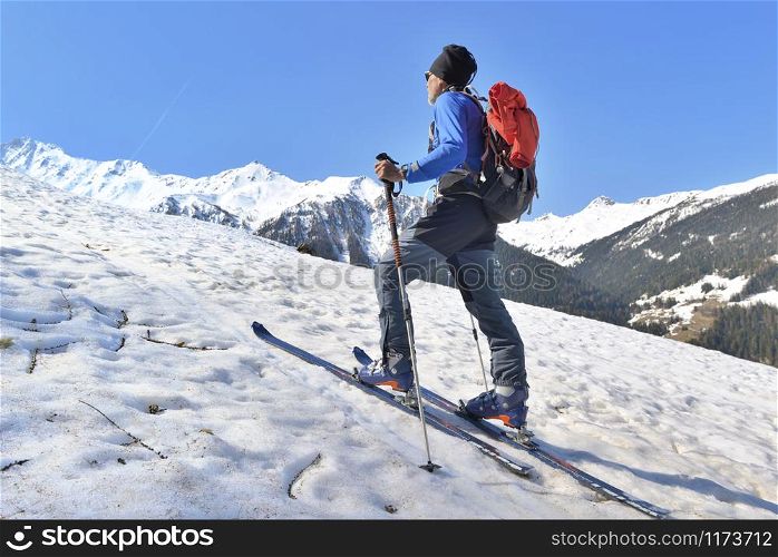 hiker in touring ski climbing snowy mountain on a sunny and warm day