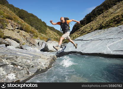 Hiker jumping across river