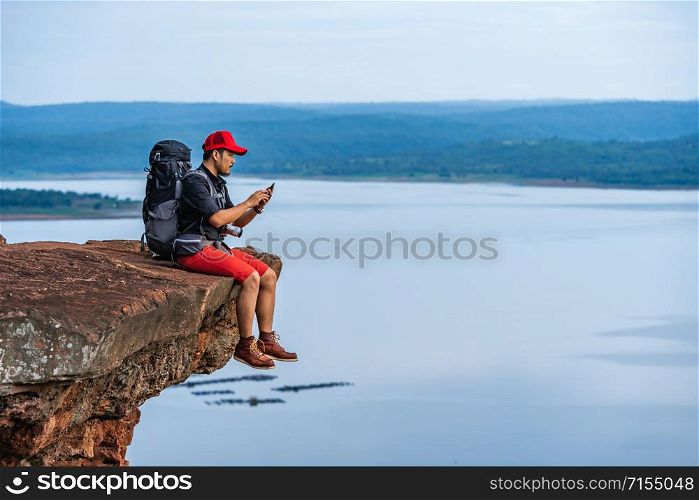 hiker man sitting and using smartphone on the edge of cliff, on a top of the rock mountain