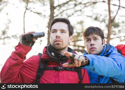Hiker showing something to friend holding binoculars in forest