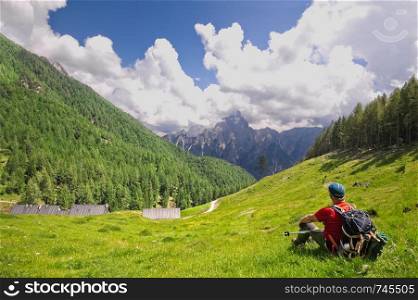 Hiker sitting on the lawn admires the view. Alps Italy