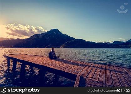 Hiker sitting on the wooden pier. Tramper looking the landscape at sunset on lake.
