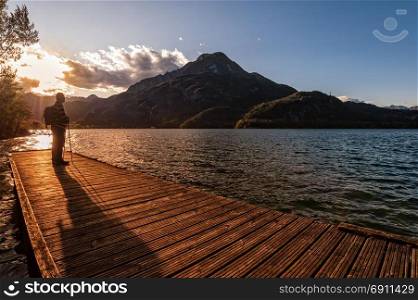 Hiker standing on dock end on lake. Tramper looking sunset over the lake.