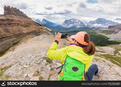 Hiker taking picture with mobile phone, rear view. Dolomite Pass, Alberta, Canada