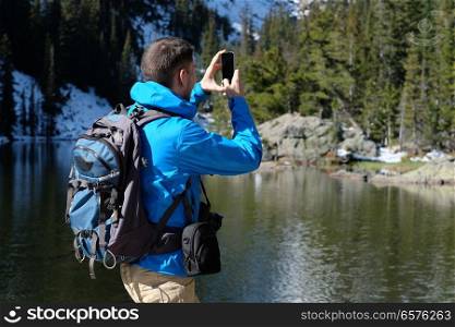 Hiker tourist with backpack taking photo with smartphone near Bear Lake at autumn in Rocky Mountain National Park. Colorado, USA. 